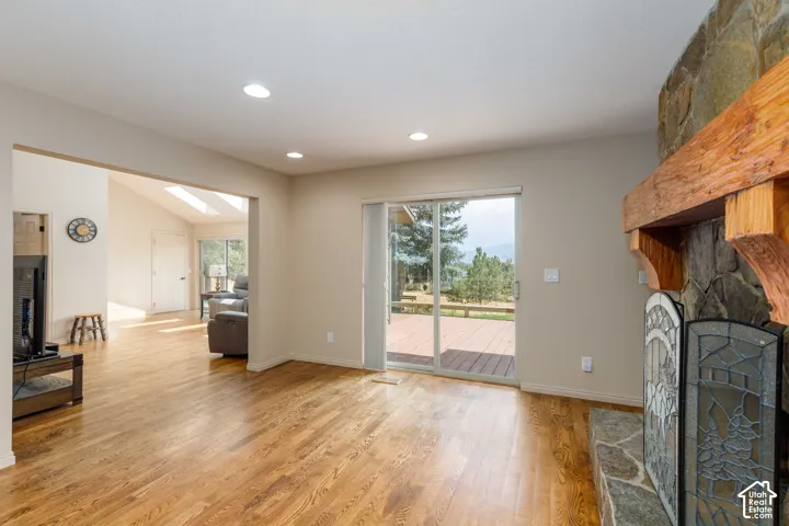 Stone fireplace with a substantial wood mantel, wood-finish flooring, recessed lighting, and a sliding glass door to an outdoor deck