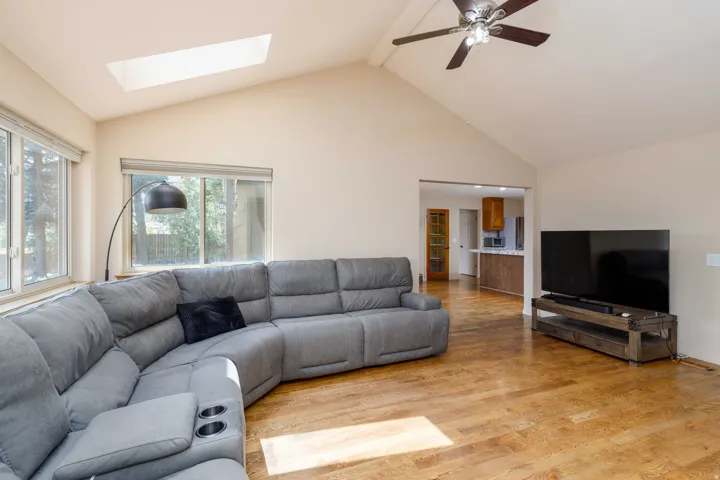 Vaulted ceiling with a skylight and ceiling fan, wood-finish flooring, and multiple windows