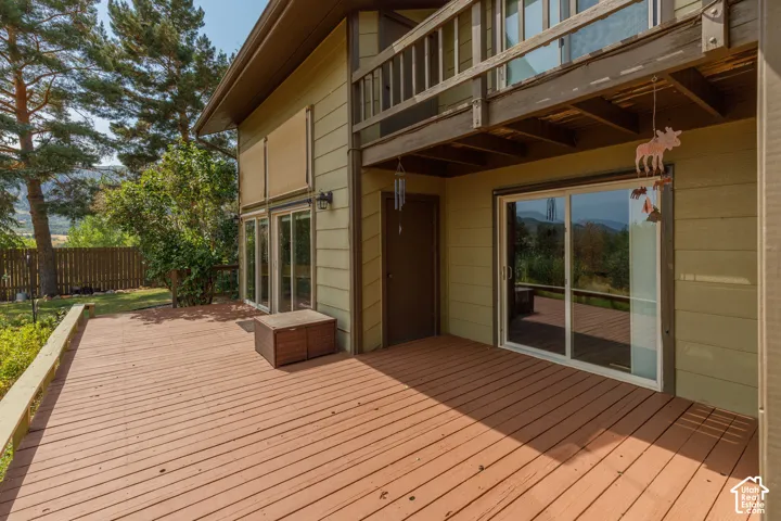 Expansive multi-level wood deck, neutral exterior siding, upper-level balcony, multiple glass sliding doors, and a natural landscape backdrop