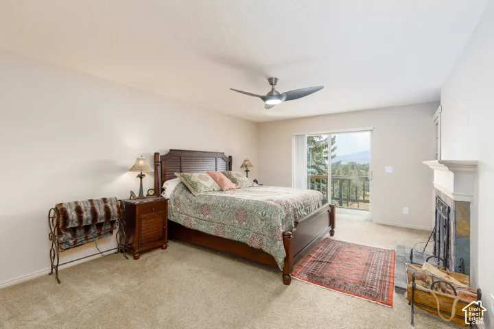 Carpeted bedroom featuring a ceiling fan, a fireplace with a stone surround and white mantel, and a sliding glass door opening to an exterior deck