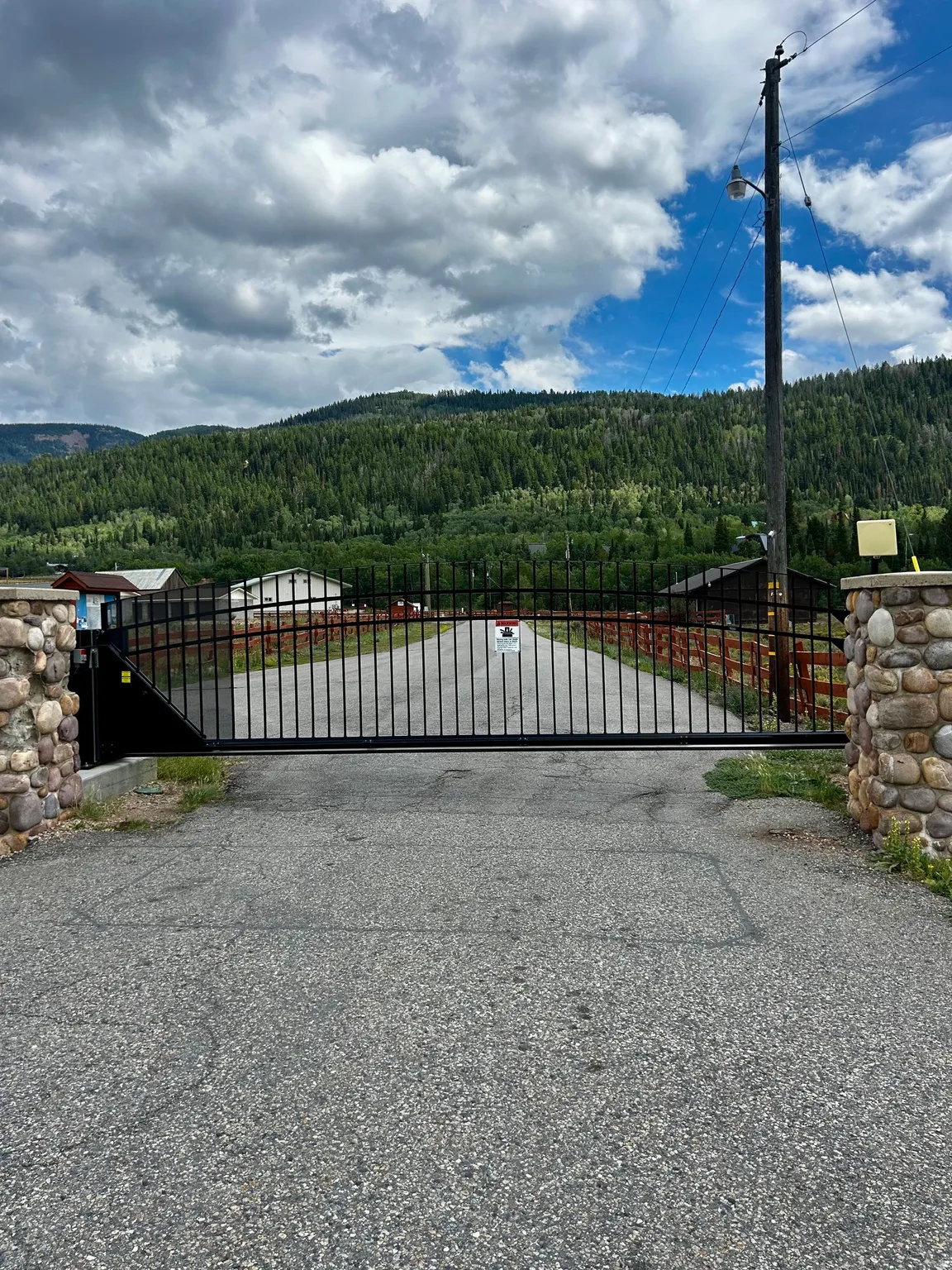 Gated entry with stone pillars and paved drive, framed by extensive hillside tree coverage