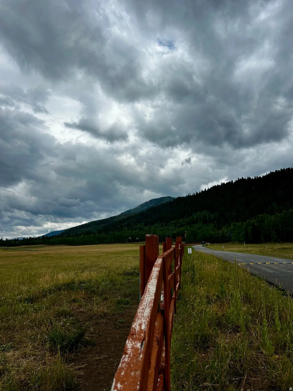 Expansive field with a rustic wooden fence, bordered by a paved road