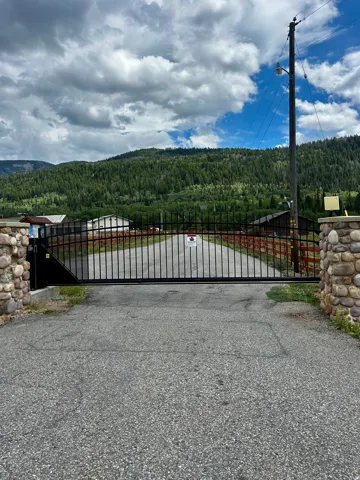 Gated entry with stone pillars and paved drive, framed by extensive hillside tree coverage
