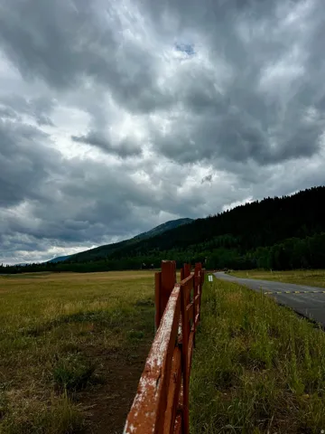 Expansive field with a rustic wooden fence, bordered by a paved road