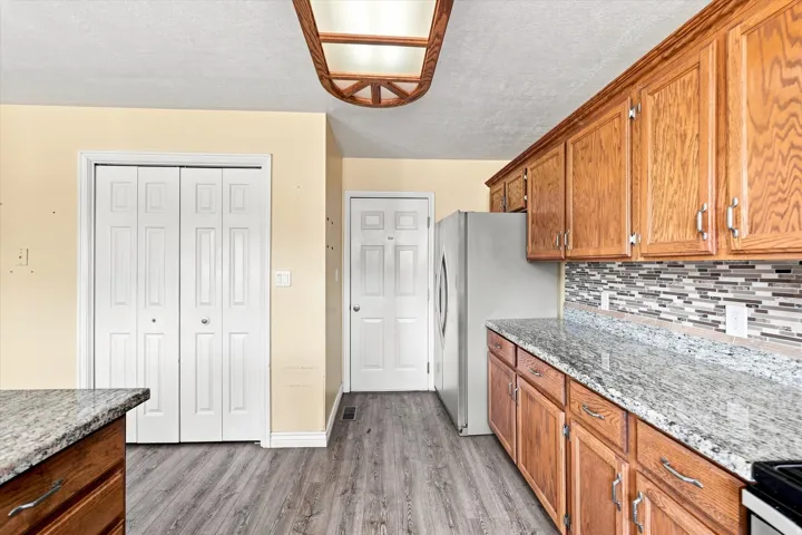 Wood-finish flooring, wood cabinetry, granite-style countertops, mosaic tile backsplash, and stainless steel appliances