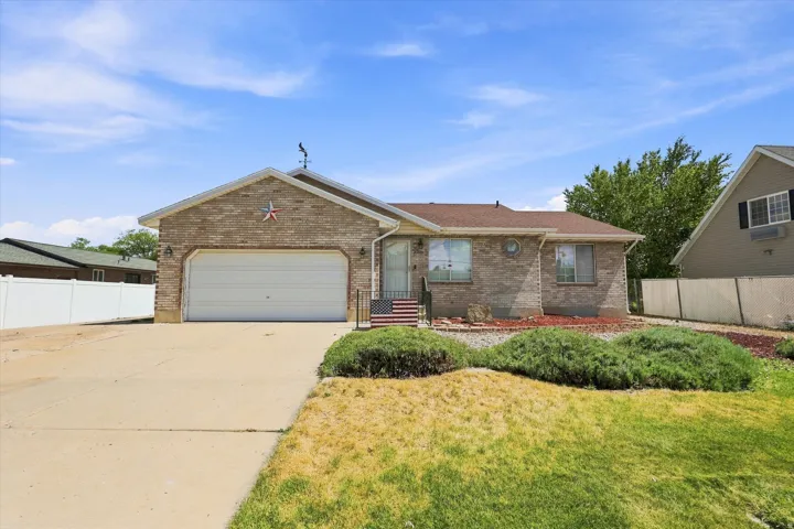 Brick exterior with an attached garage, paved driveway, and mature landscaping