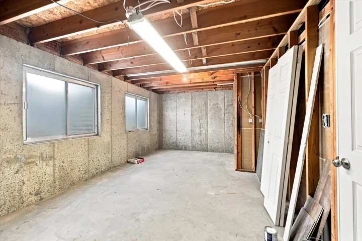 Unfinished concrete flooring with exposed wood joist ceiling and two frosted windows