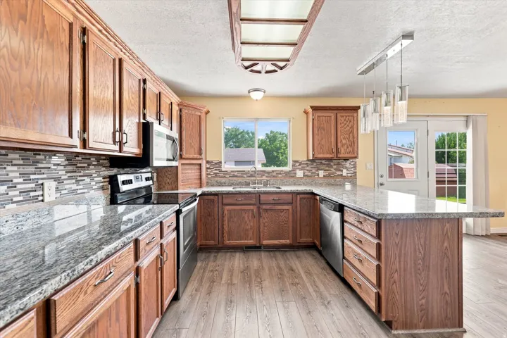 Kitchen featuring wood-finish cabinetry, granite countertops, tile backsplash, stainless steel appliances, and wood-finish flooring
