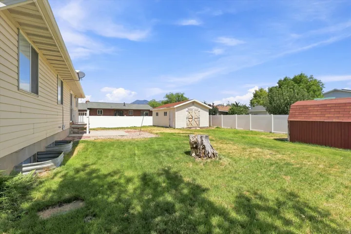 Expansive backyard featuring a manicured lawn, two storage sheds, and a white privacy fence