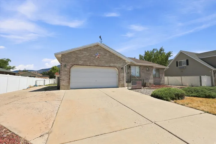 Brick facade with an attached garage, paved driveway, and mature landscaping