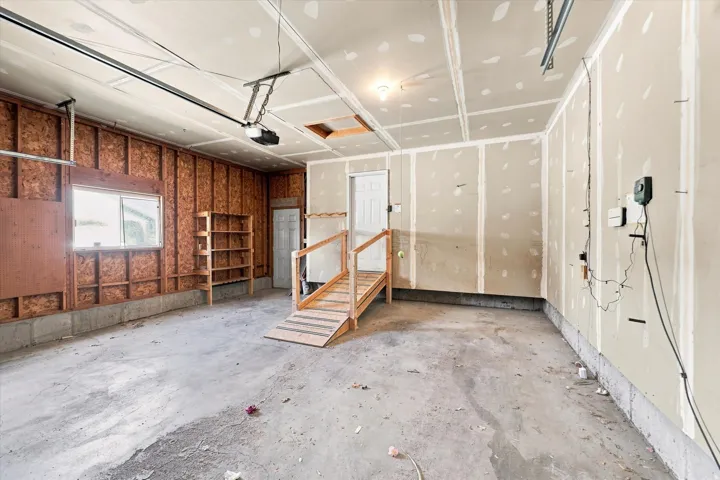 Attached garage with exposed wood framing, concrete flooring, and built-in shelving
