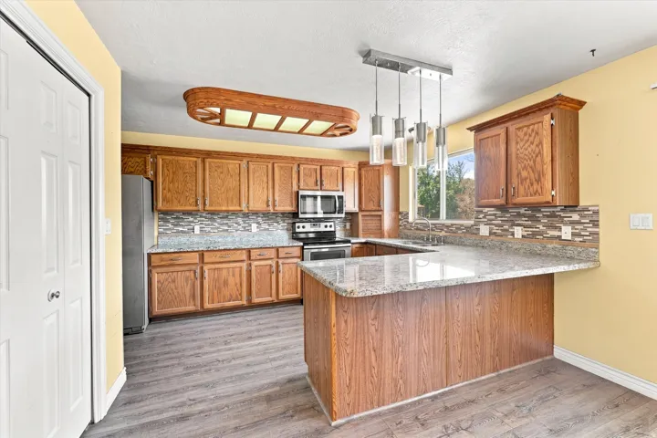 Kitchen featuring wood-finish cabinetry, granite countertops, tile backsplash, and stainless steel appliances