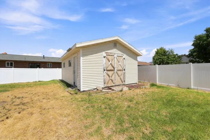 Exterior storage shed with double barn doors, surrounded by a white privacy fence