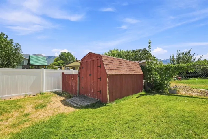 Expansive green lawn featuring a red barn-style shed with a shingled roof, a white privacy fence, and a chain-link fence with established plantings