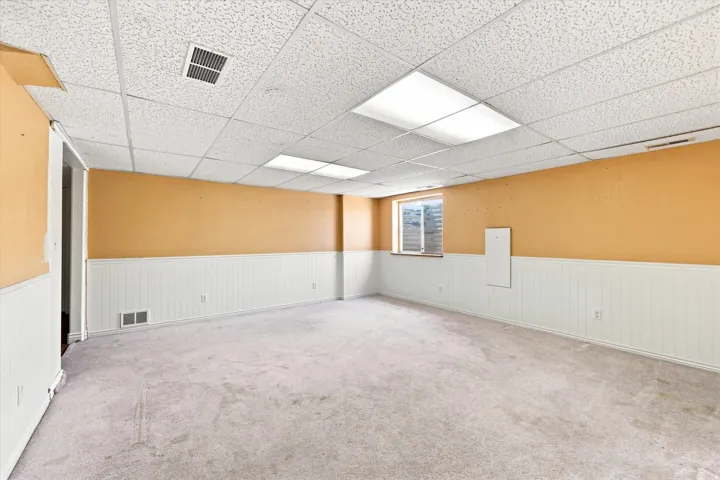 Recessed lighting fixtures, drop ceiling, window, white wainscoting, and carpeted flooring