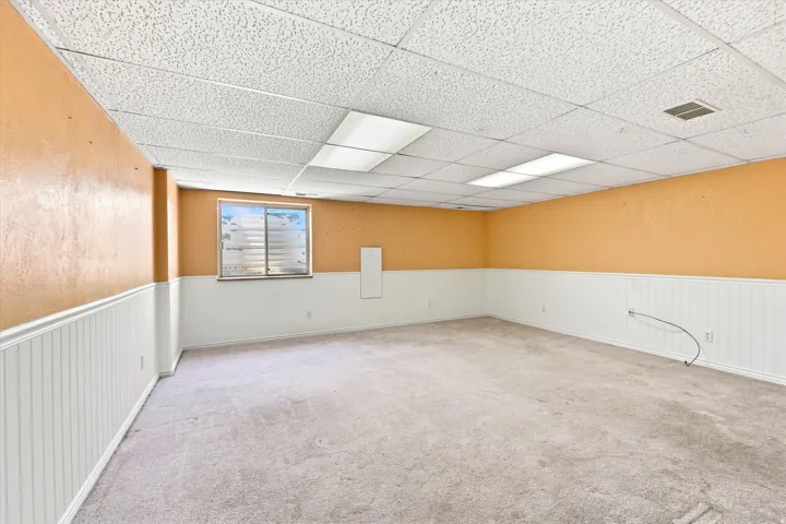 Carpeted room featuring a drop ceiling with recessed lighting, wainscoting, and a window