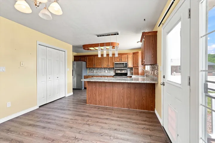 Wood-finish flooring throughout, with a kitchen featuring wood cabinetry, stainless steel appliances, a tiled backsplash, and light-toned countertops
