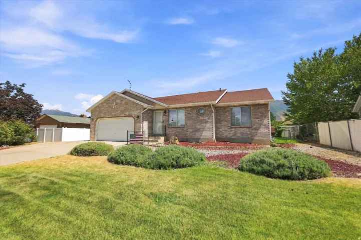 Brick exterior featuring a two-car garage, mature landscaping, and a pitched roof