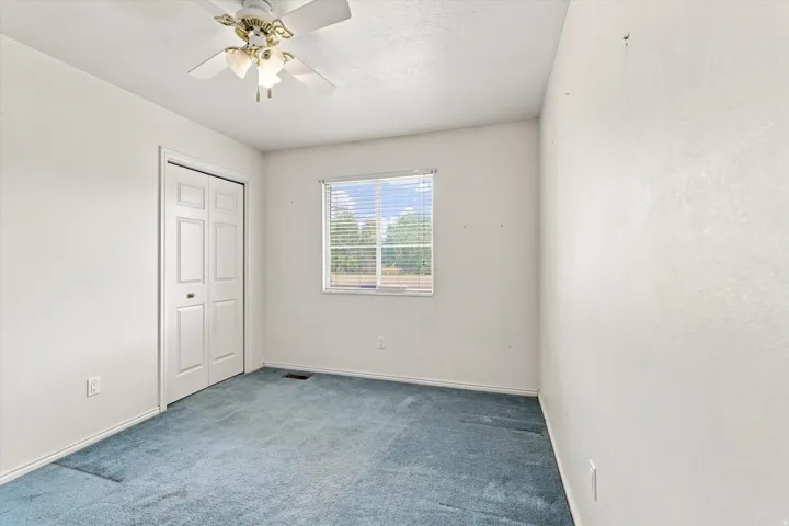 Room featuring a window with blinds, bi-fold closet doors, and a ceiling fan with light fixture