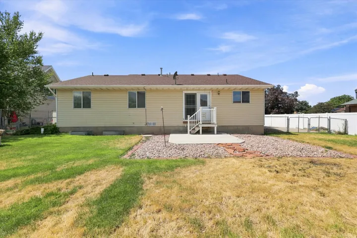 Rear exterior featuring light-colored siding, a brown shingle roof, and a white deck leading to a concrete patio