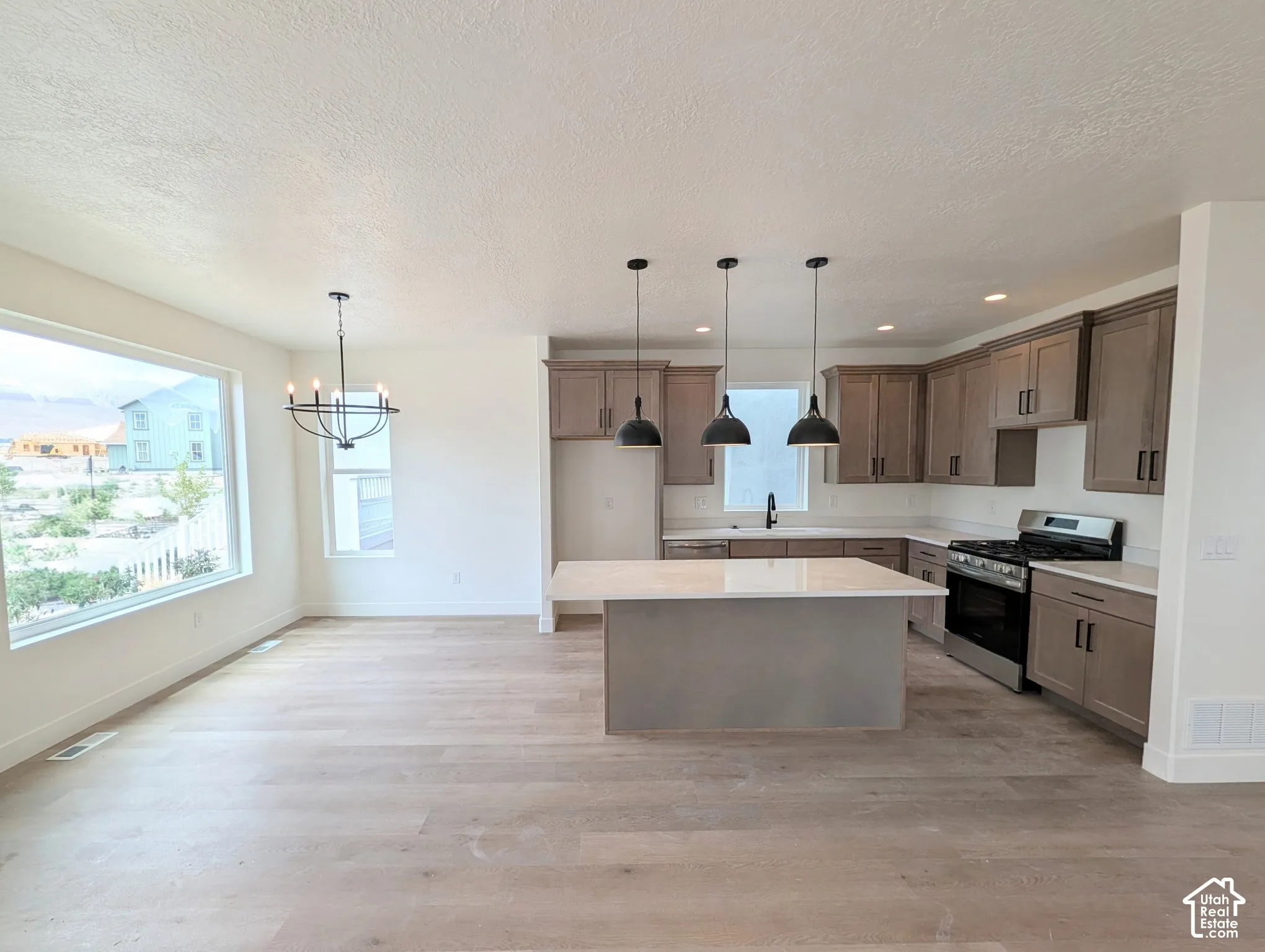 Open concept living area with wood-finish flooring, a contemporary chandelier, a kitchen island, pendant lighting, and stainless steel appliances