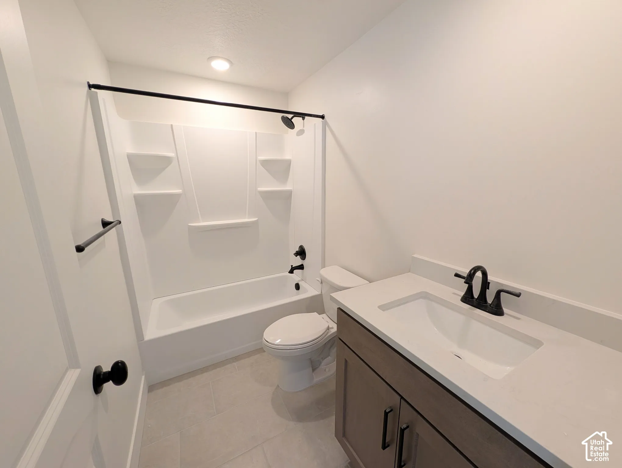 Bathroom with a white bathtub and shower surround, dark bronze fixtures, a vanity with a white countertop, and a built-in sink