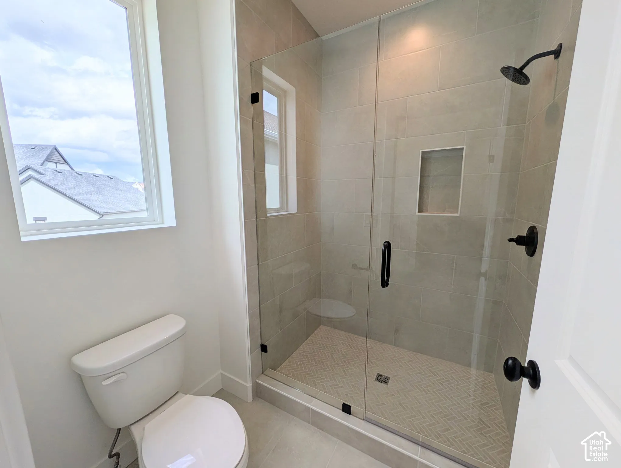 Primary Glass-enclosed shower with matte black fixtures, integrated shower niche, and herringbone-patterned shower floor