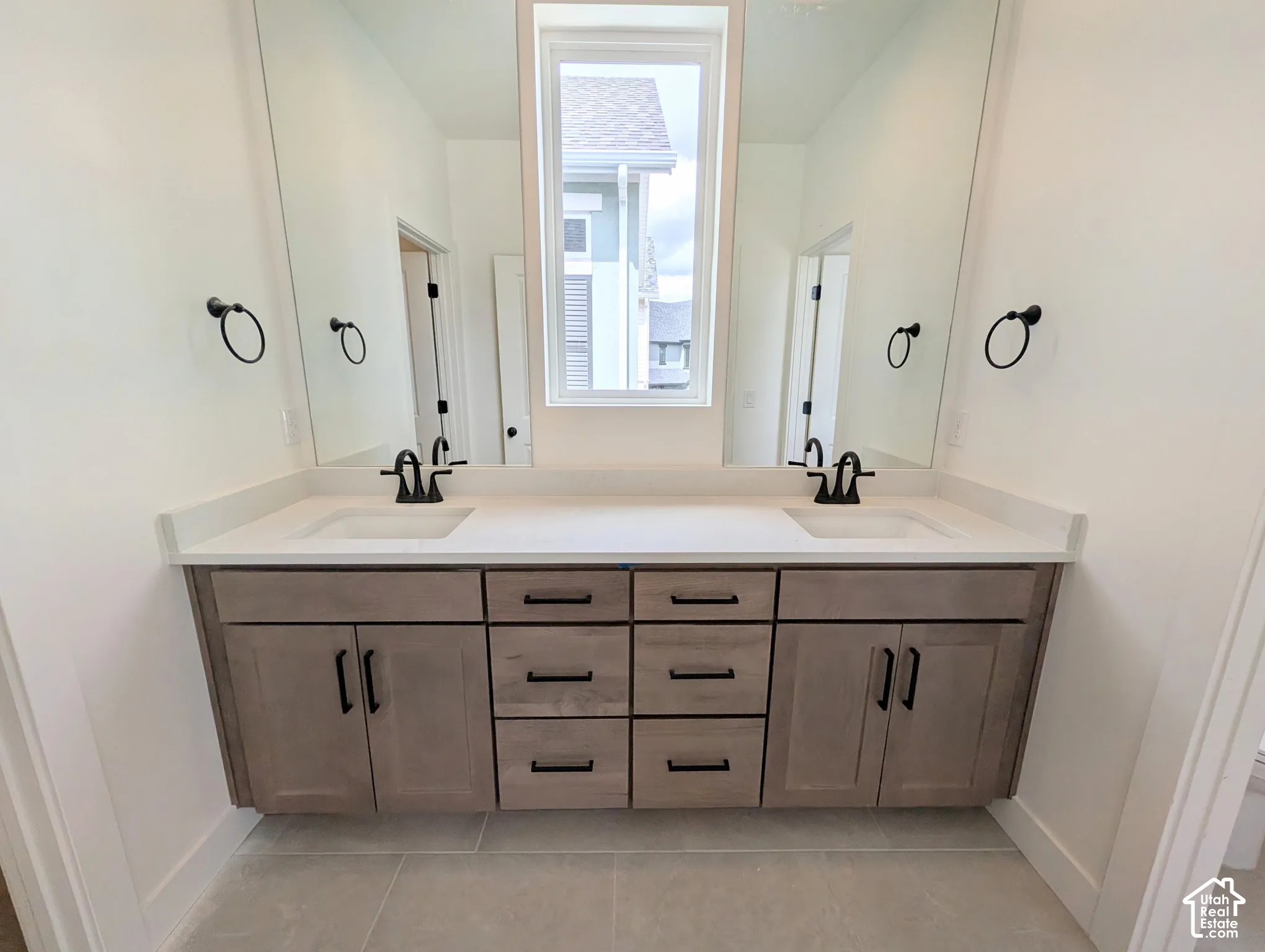 Primary bathroom dual vanity with wood-finish cabinetry, integrated sinks, white countertops, and matte black fixtures
