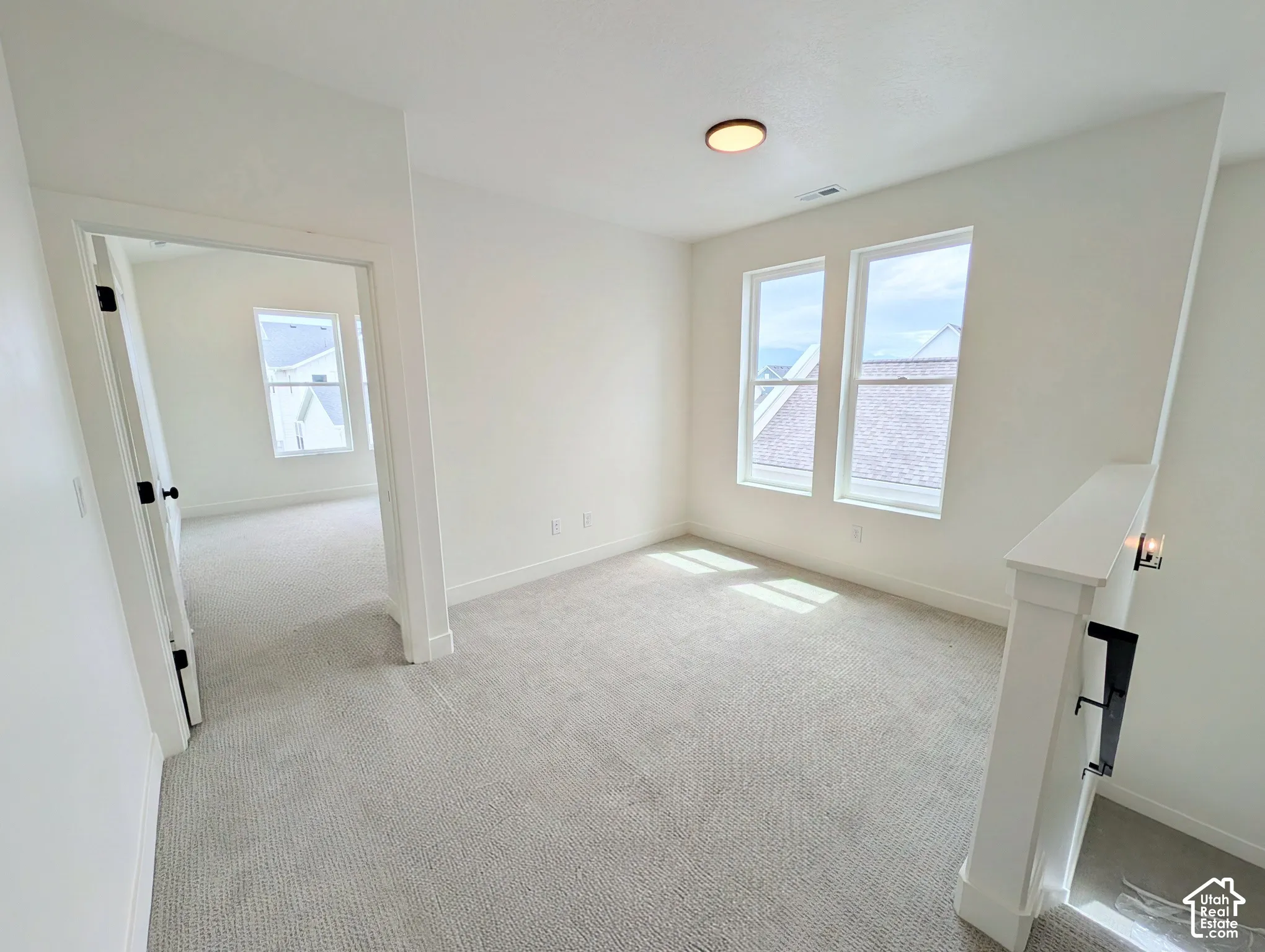 White walls, light-toned carpet flooring, two windows, and a flush-mount ceiling light
