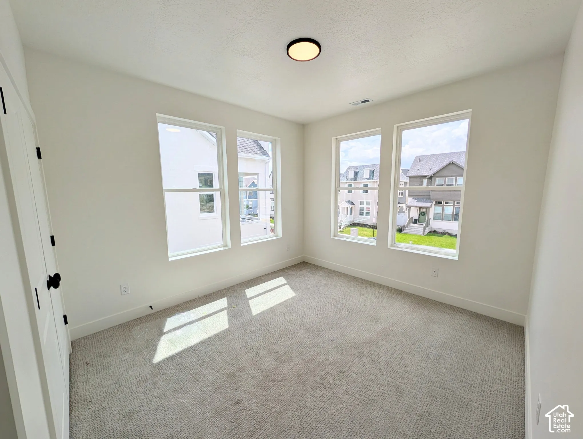 Multiple large windows, neutral wall finishes, light-toned carpet, recessed ceiling light fixture, white interior door with black hardware