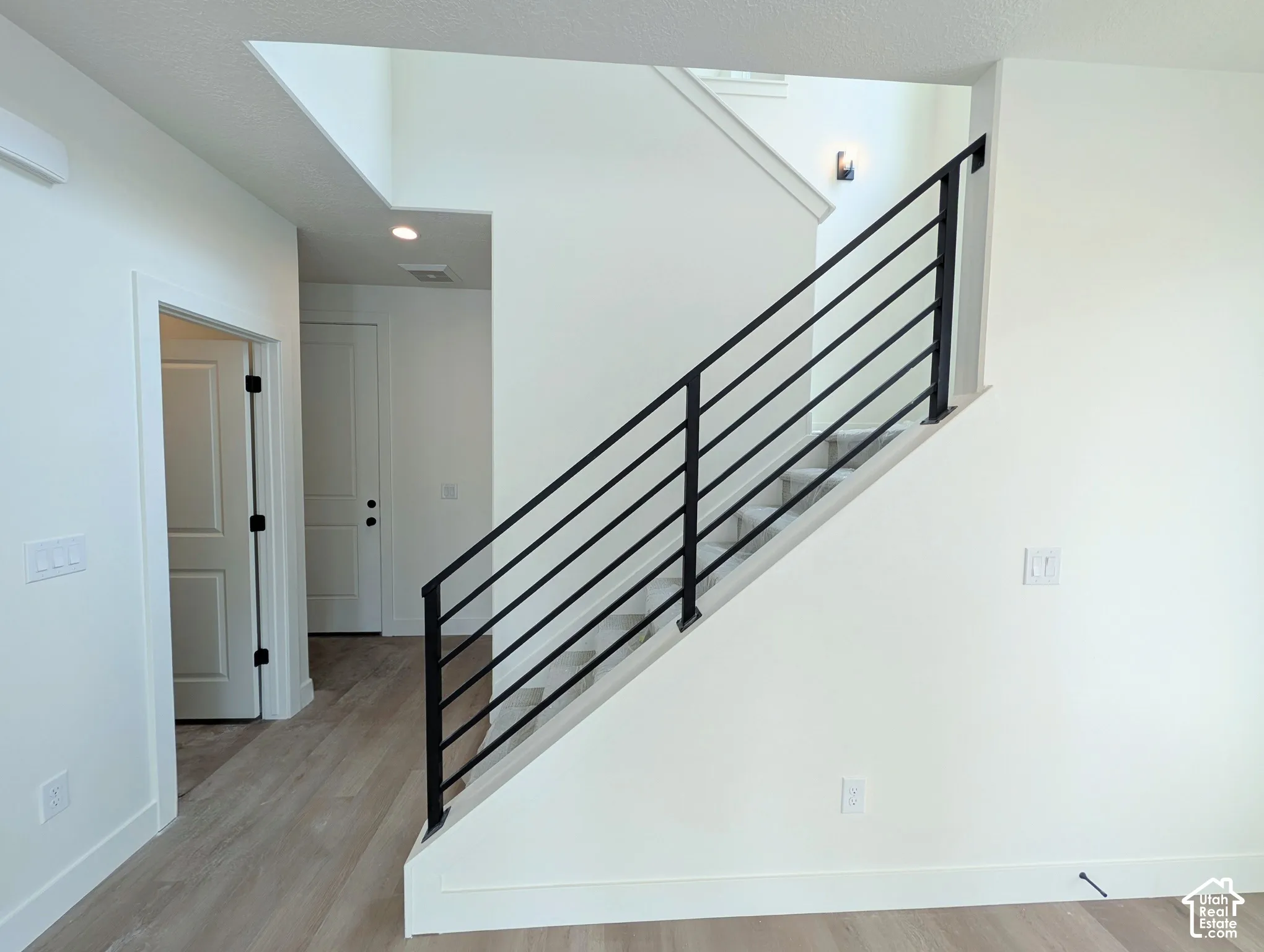 Modern horizontal metal stair railing, light wood-finish flooring, recessed ceiling lighting, contemporary wall sconce, and clean white interior doors