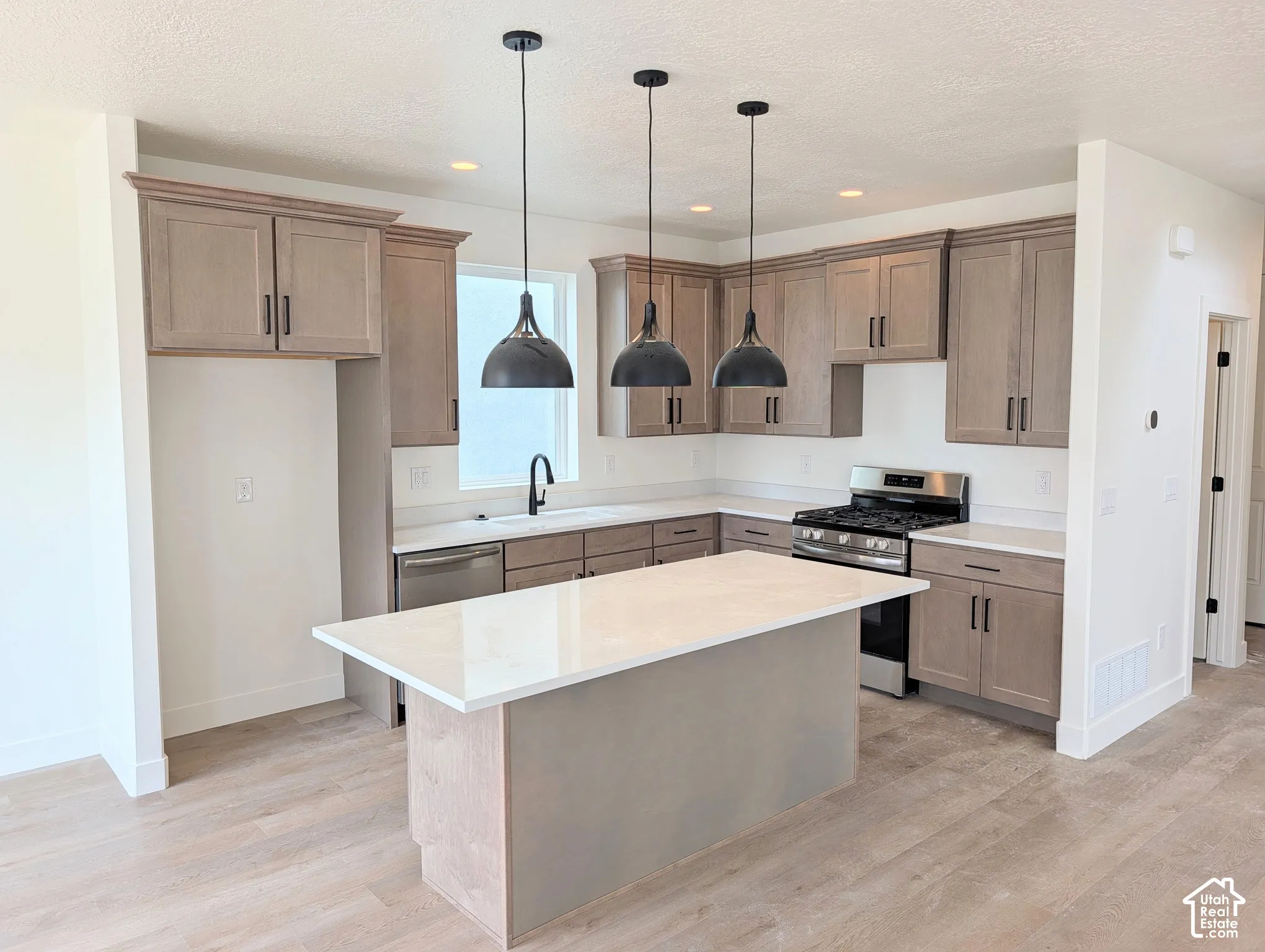Contemporary kitchen featuring a center island, wood-finish flooring, light wood cabinetry, stainless steel appliances, and pendant lighting