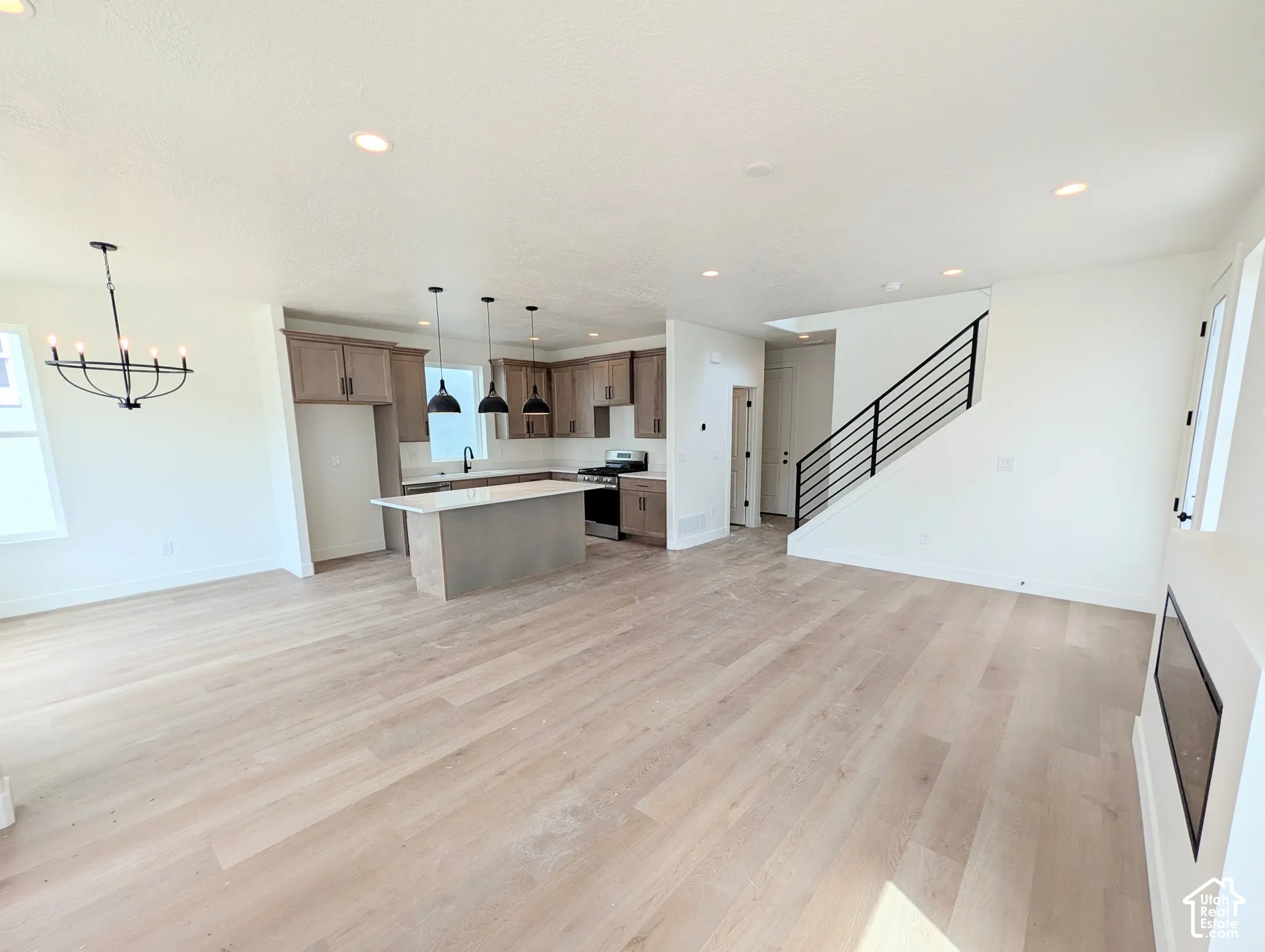 Open-concept living space featuring wood-finish flooring, recessed lighting, a modern kitchen with a center island, and a staircase with a black metal railing