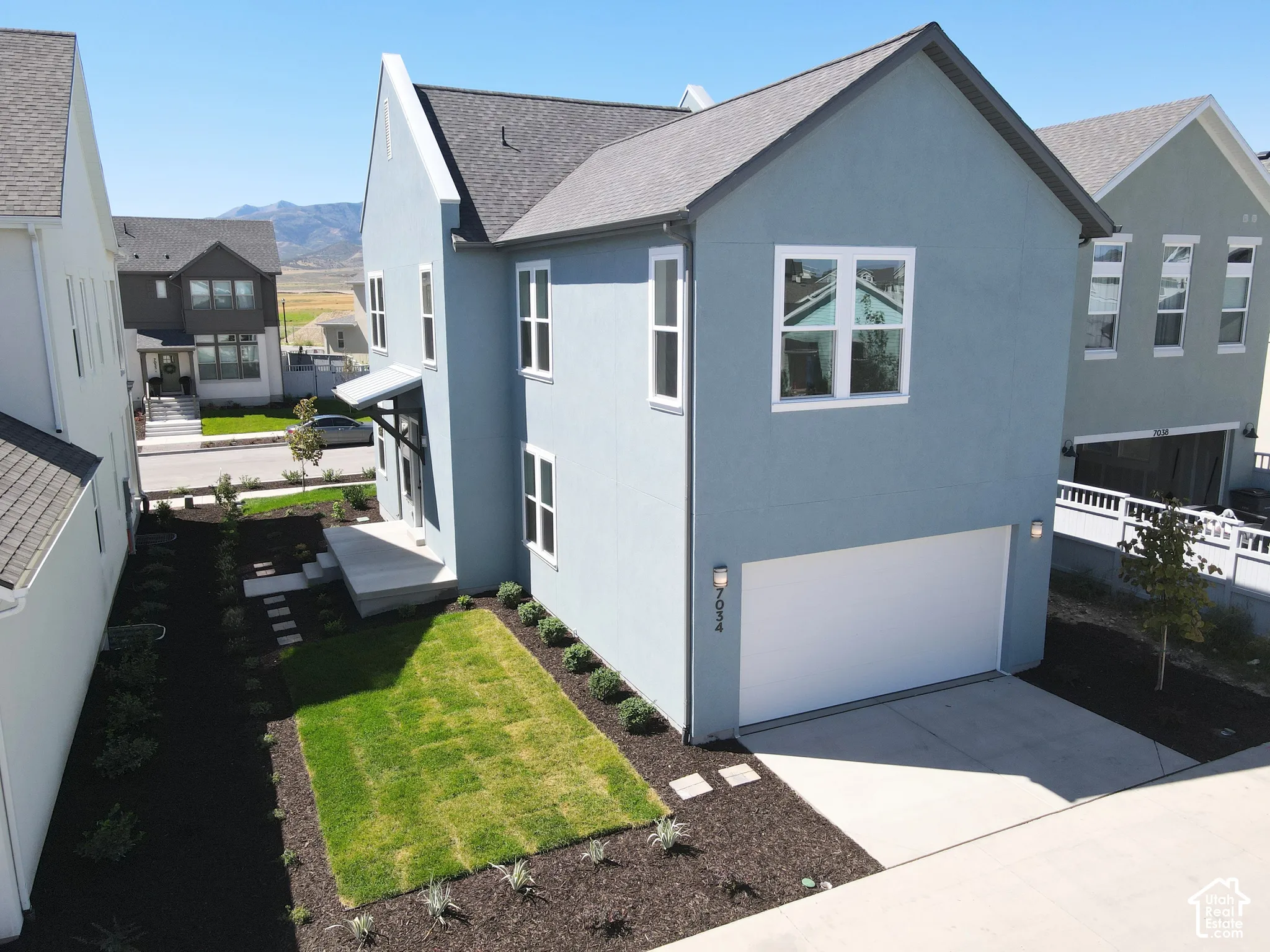 Modern two-story residence with a light blue exterior, featuring a white garage door and a front porch with a dark-colored awning