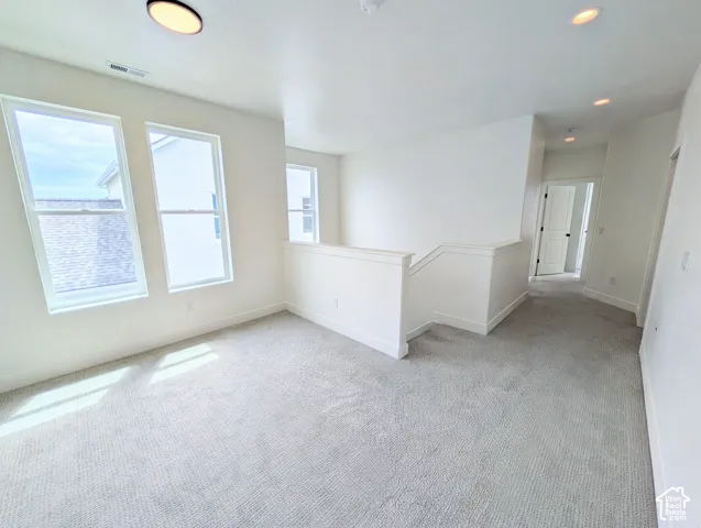 Upper-level space with plush carpeting, multiple windows, a staircase with a white railing, and recessed ceiling lighting