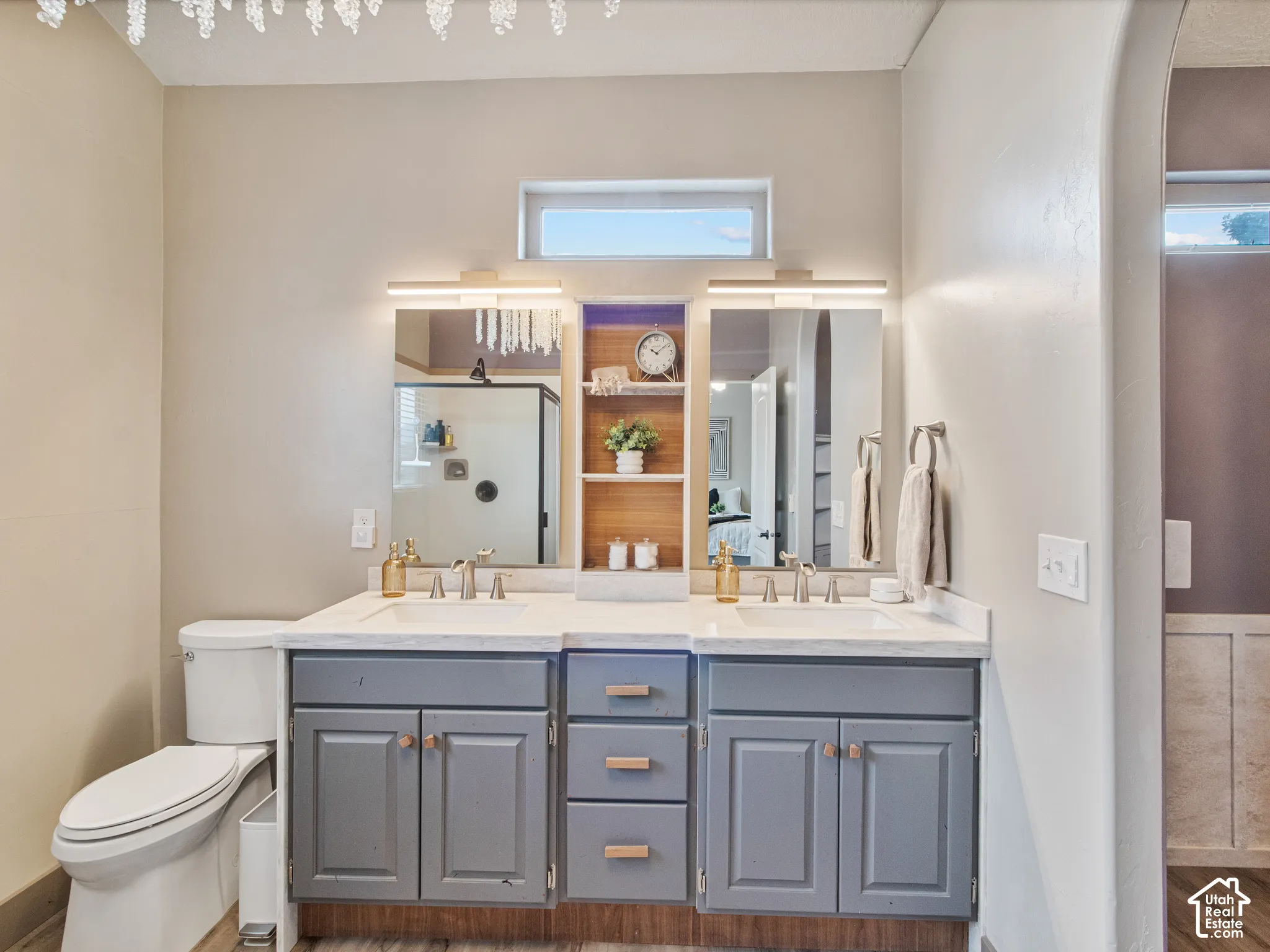 His & Her basin vanity with undermount sinks and modern fixtures, gray cabinetry with wood-finish hardware, built-in shelving, and a decorative light fixture