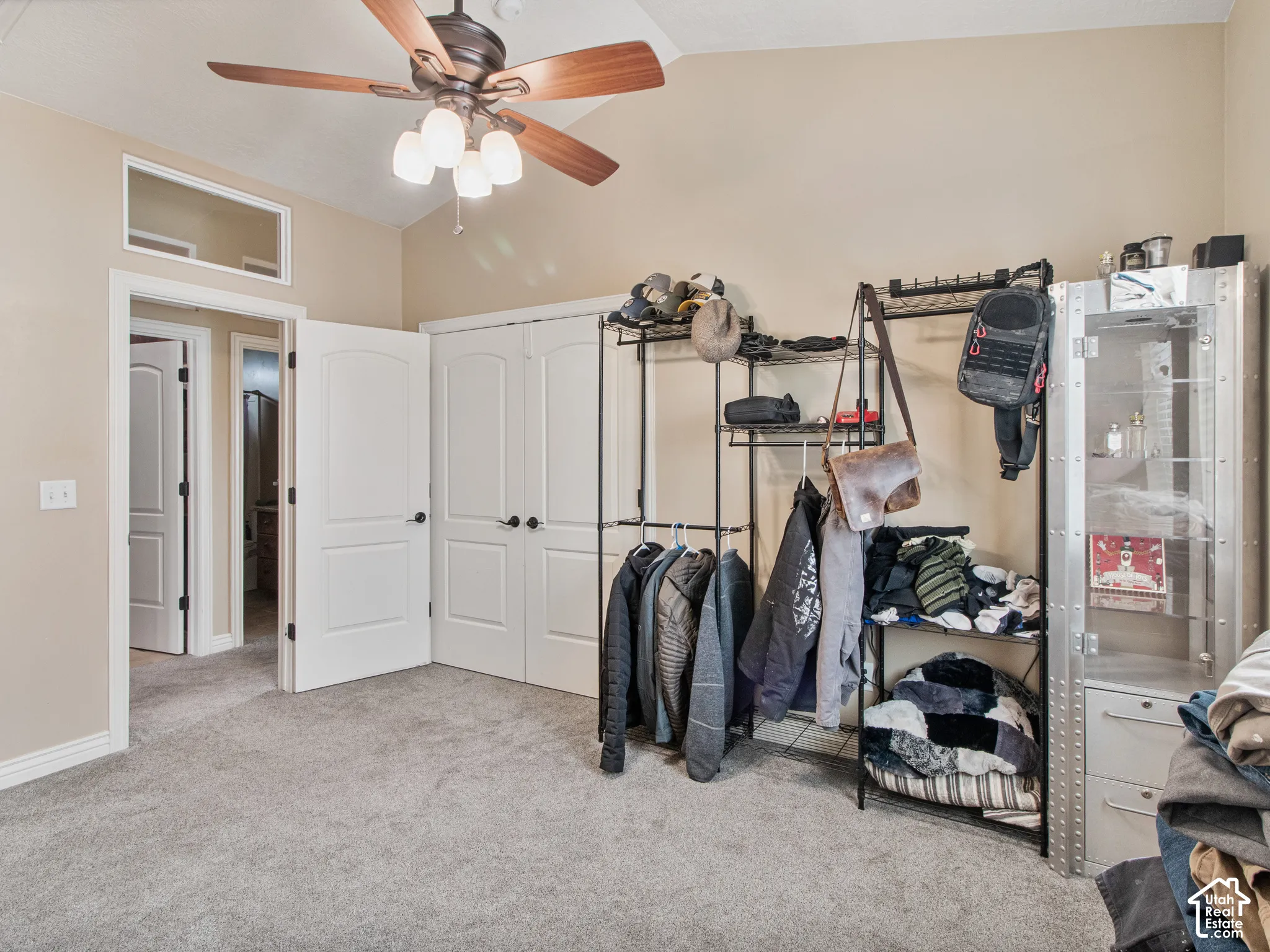 Vaulted ceiling with a ceiling fan, light gray carpeting, and two white bi-fold closet doors
