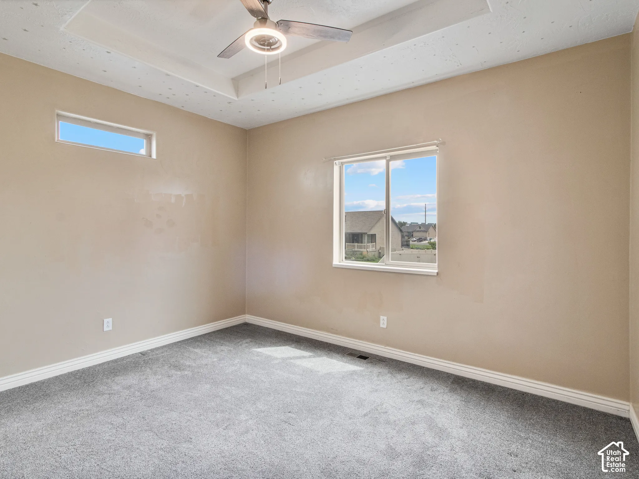 Tray ceiling with a ceiling fan, neutral wall tones, and gray carpeting
