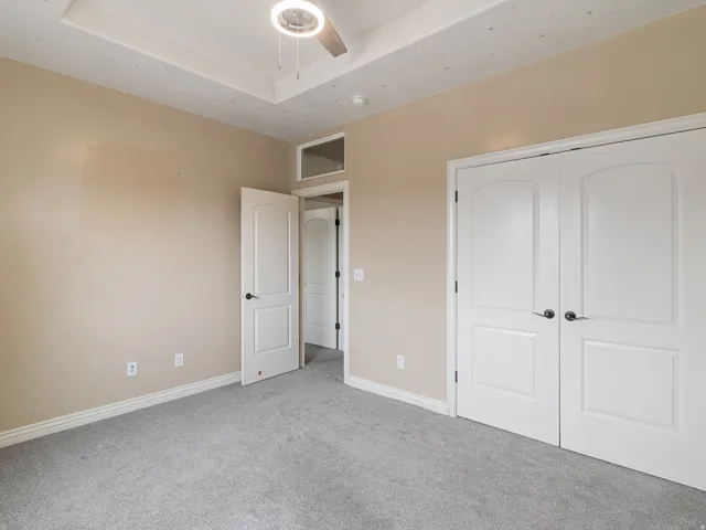 Tray ceiling with a ceiling fan and integrated lighting, neutral wall tones, gray carpeting, white bi-fold closet doors, and white trim