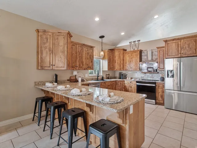 Spacious Kitchen featuring wood cabinetry, light granite countertops, stainless steel appliances, a tile backsplash, and recessed lighting
