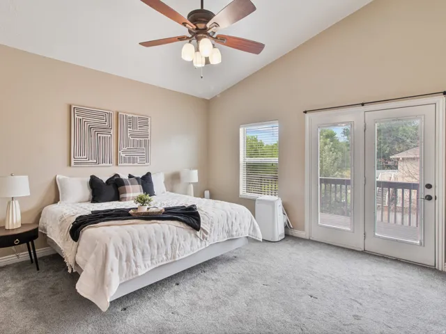 Master bedroom with vaulted ceiling with a ceiling fan, carpeted flooring, window with blinds, and French doors leading to an outdoor deck