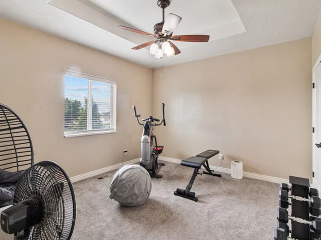Recessed ceiling with a ceiling fan, window with blinds, and neutral wall paint