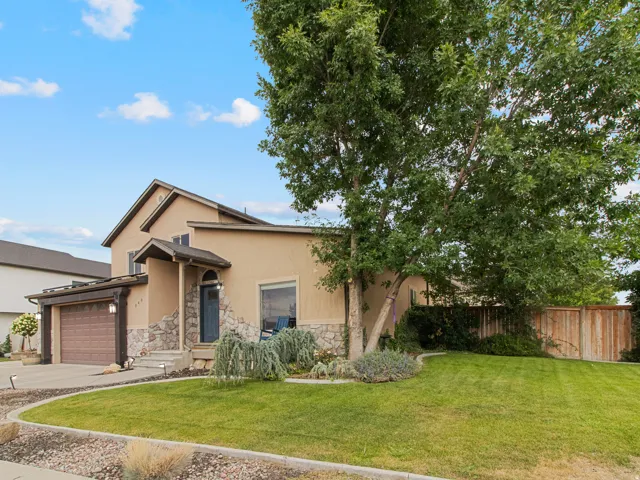 Stucco exterior with stone accents, attached two-car garage, mature landscaping, concrete driveway, and covered entry