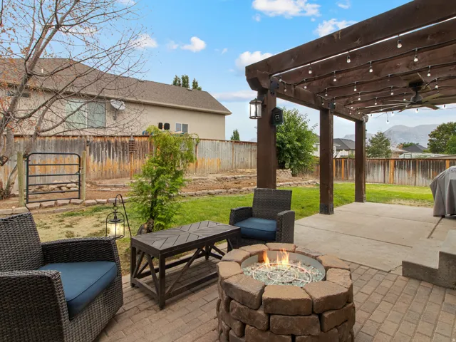 Expansive backyard featuring a stone-clad fire pit, brick paver patio, wood pergola with built-in lighting, and a manicured lawn