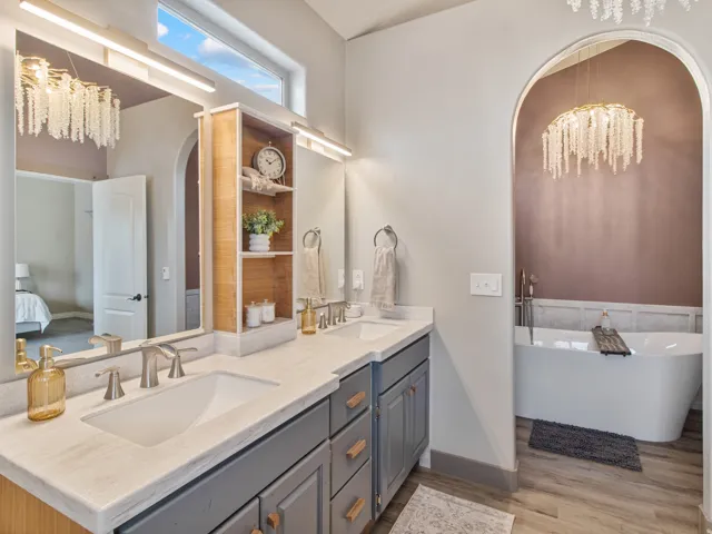 Dual vanity with undermount sinks and modern faucets, integrated storage cabinetry, built-in shelving, freestanding tub, and wood-finish flooring
