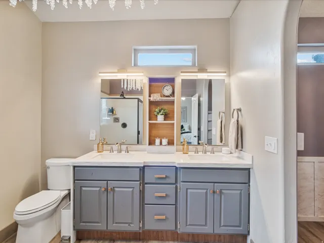 His & Her basin vanity with undermount sinks and modern fixtures, gray cabinetry with wood-finish hardware, built-in shelving, and a decorative light fixture