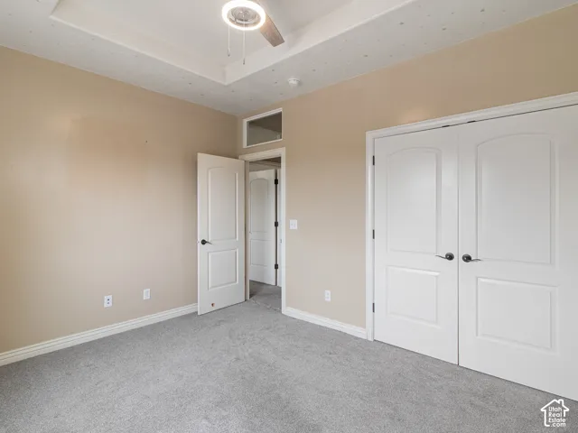 Tray ceiling with a ceiling fan and integrated lighting, neutral wall tones, gray carpeting, white bi-fold closet doors, and white trim