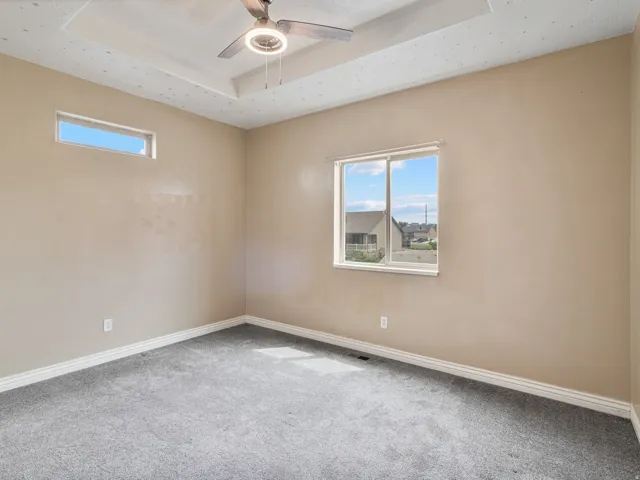 Tray ceiling with a ceiling fan, neutral wall tones, and gray carpeting