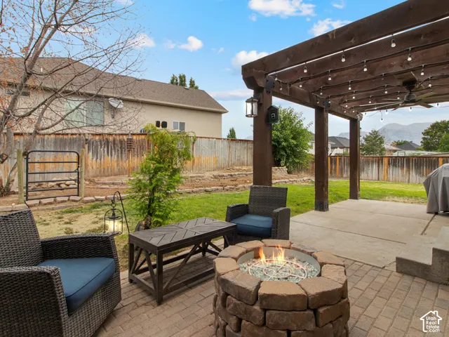 Expansive backyard featuring a stone-clad fire pit, brick paver patio, wood pergola with built-in lighting, and a manicured lawn