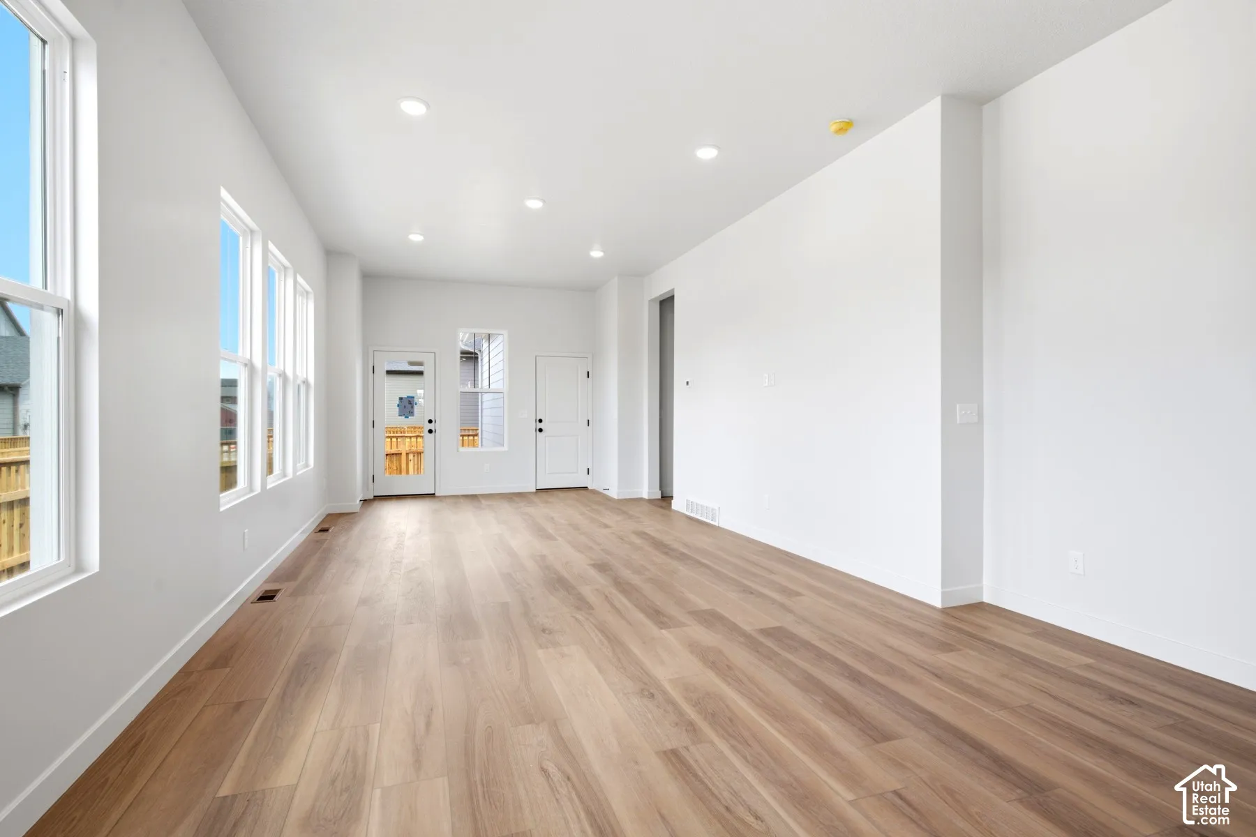 Expansive open-concept room featuring wide-plank wood-finish flooring, recessed lighting, and multiple large windows